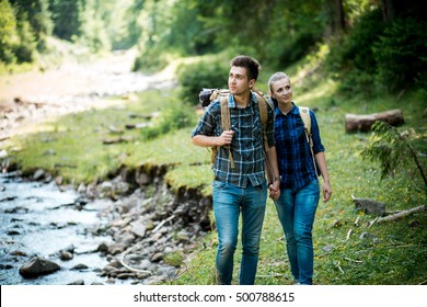 Man and woman tourists walking hand in hand through the woods in the mountains by the river