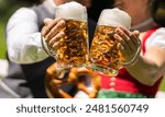 man and woman in traditional Bavarian attire clink large frothy beer mugs together, with a pretzel visible in the background at oktoberfest or beer garden in munich germany, 