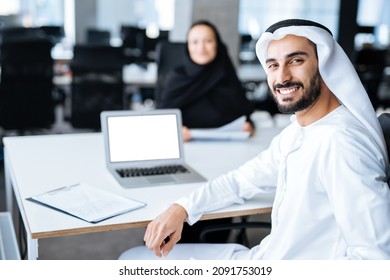 Man and woman with traditional clothes working in a business office of Dubai. Portraits of  successful entrepreneurs businessman and businesswoman in formal emirates outfits. Concept about middle east