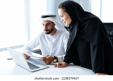 Man and woman with traditional clothes working in a business office of Dubai. Portraits of  successful entrepreneurs businessman and businesswoman in formal emirates outfits. 