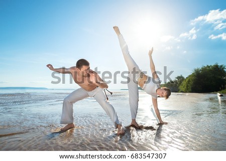 A man and a woman train capoeira on the beach - concept about people, lifestyle and sport.