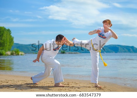 A man and a woman to train capoeira on the beach. - concept about people, lifestyle and sport. Male coach of capoeira trains his pupil. Man and woman play staged fight.