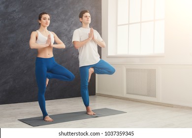 Man And Woman Training Yoga In Tree Pose. Young Couple Making Relaxing Exercise, Copy Space. Partner Yoga, Balance Concept