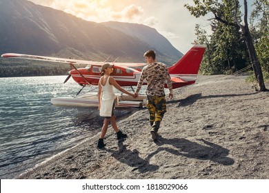 Man And Woman Travel By Private Plane On Alaska Adventure Trip. Hydroplane Parked On A Mountain Lake. 