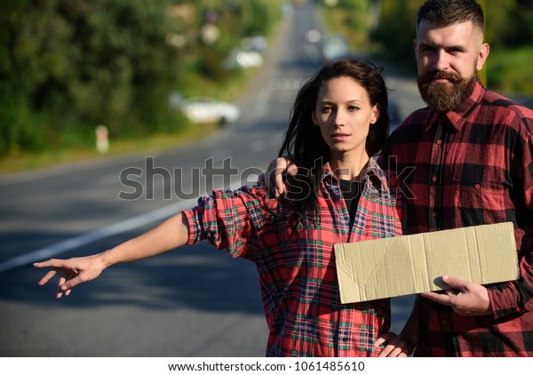 Man and woman try to stop car with cardboard sign\
and gesture. Adventure and hitchhiking concept. Couple with tired\
faces travel by auto stop. Couple in love travelling by\
hitchhiking, copy space.