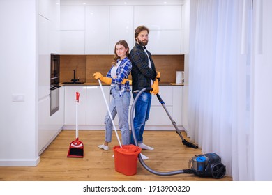 man and woman use vacuum cleaner and mop, couple of cleaners in uniforms work together modern center apartment full length interior.