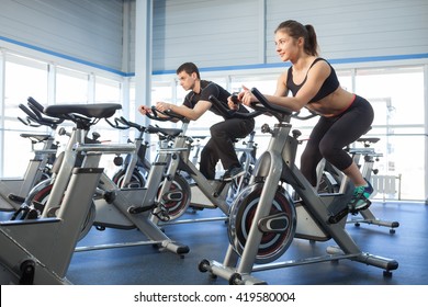 Man And Woman Using Cycling Exercise Bikes At The Gym