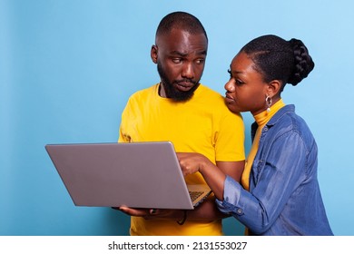 Man And Woman Using Laptop Computer In Front Of Camera. African American Couple Browsing Internet And Social Media App On Pc, Looking At Screen Over Blue Background. People Working