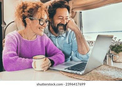 Man and woman using laptop inside camper van during travel lifestyle van life. Happy couple smile in front of a computer during rv motor home vacation. Smart working and digital nomad concept day - Shutterstock ID 2396417699