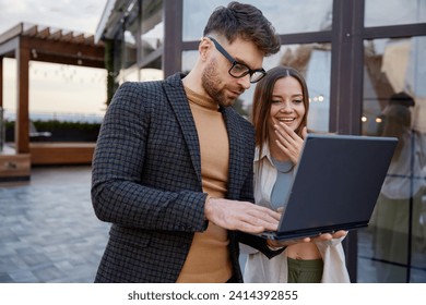 Man and woman using laptop standing together on roof terrace - Powered by Shutterstock