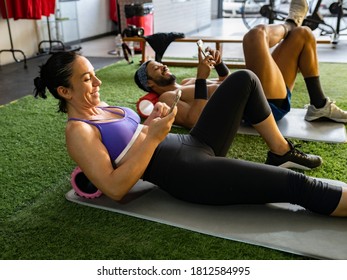 man and woman using mobile phone after exercising in gym