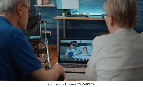 Man And Woman Using Online Call To Talk To Doctor And Child On Laptop. Retired People Talking To Medic And Little Girl In Hospital On Remote Video Conference For Telemedicine And Telehealth.