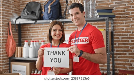 Man and woman volunteers standing together holding paper with thank you message at charity center