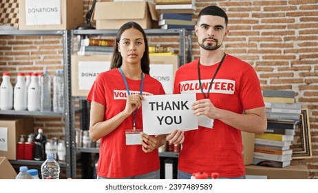 Man and woman volunteers standing together holding thank you paper at charity center