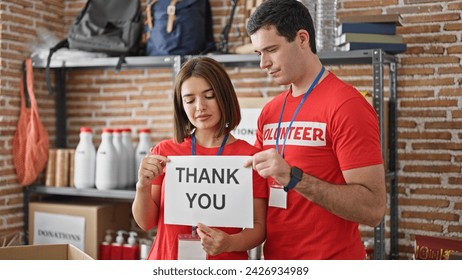 Man and woman volunteers standing together holding paper with thank you message at charity center