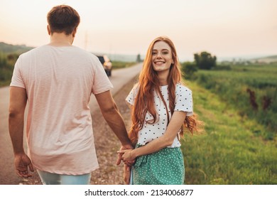 Man and woman walking on the side of the road holding hands, woman turning her face to the camera, smiling. Beautiful young girl. Summer vacation. Pretty young