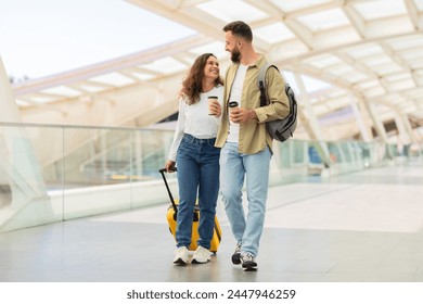 Man and Woman Walking Through Airport With Luggage And Takeaway Coffee, Happy Young Couple Going To Flight Departure Gate And Chatting, Enjoying Travelling Together, Copy Space - Powered by Shutterstock