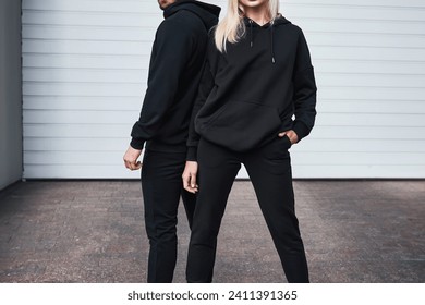 Man and woman wear black hoodies.  A fashion template for print and branding on hoodie. trendy couple on the street wearing casual apparel with no face visible. No logo sweater and pullover with hood.