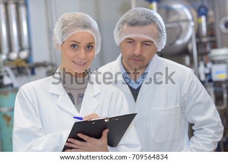 Man and woman wearing hair nets making notes on clipboard