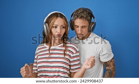 Man and woman wearing headphones against blue background, sharing a moment of connection with a subtle dance move