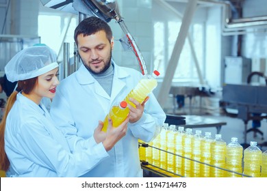 A man and a woman in white overalls against the background of a line for the production of sunflower and olive oil with bottles of oil in their hands. Quality control in production - Powered by Shutterstock