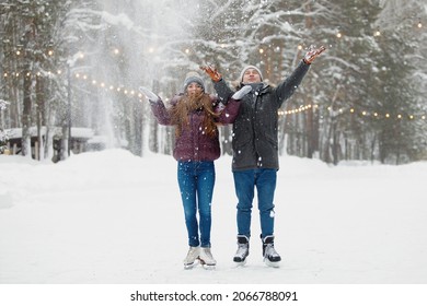 Man and woman in winter clothes throw snow at the skating rink in the park. Jacket with a hood, knitted hat, snowy forest. Healthy lifestyle. Sports concept. Selective focus.