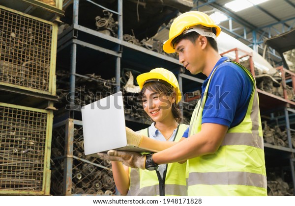 Man and woman\
work together, diversity of Asian engineer workers stand, laugh and\
using laptop in\
factory-warehouse
