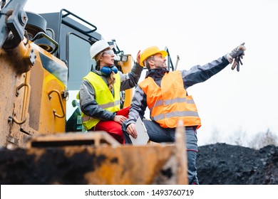 Man and woman as workers on excavator in quarry pointing at things