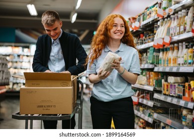 Man and woman working at a supermarket restocking the shelves. Grocery store employees at work. - Powered by Shutterstock