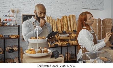 Man and woman working together in a bakery, surrounded by pastries and bread, wearing aprons and using a tablet and touchscreen in a modern indoor setting - Powered by Shutterstock