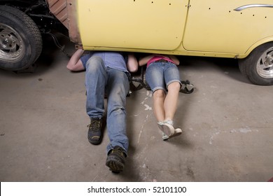 A Man And Woman Working Under A Car Together With Their Legs Sticking Out.