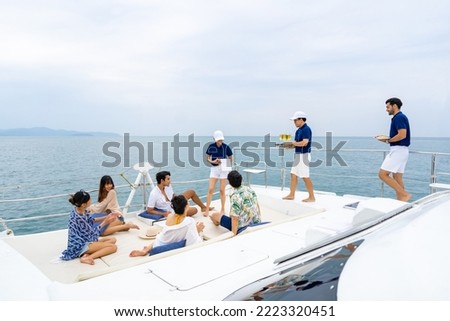 Man and woman yacht crew in uniform serving fruit and champagne to passenger tourist while luxury catamaran boat yacht sailing in the ocean on summer vacation. Cruise ship service occupation concept.
