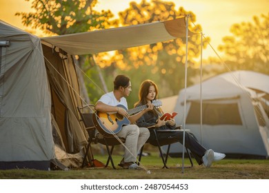 Man and woman young adult couple in nature they are sitting playing guitar, read book together for weekend activities and outdoor pursuit. Beautiful sunset above mountains, the forest at orange sunset - Powered by Shutterstock