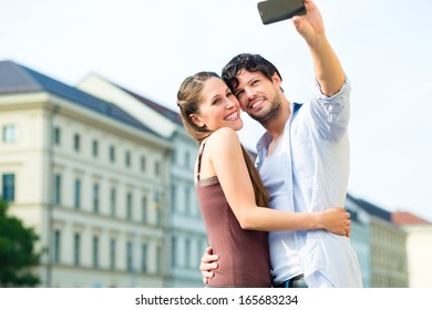 Man And Woman Or Young Couple Making Trip As Tourists In Munich And Making Snapshot With The Smartphone Or Phone