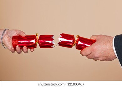 A Man And Womans Hands Pulling A Red Christmas Cracker.