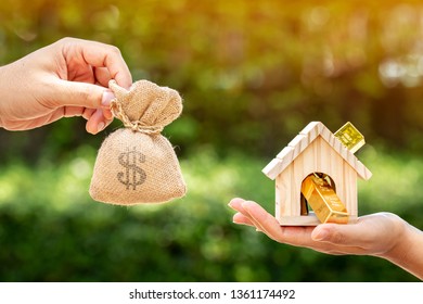 Man and women hand hold a home and gold bar and a money bag put together on sunlight in the public park, Saving money for buy a new house or loan for plan business investment of real estate concept. - Shutterstock ID 1361174492