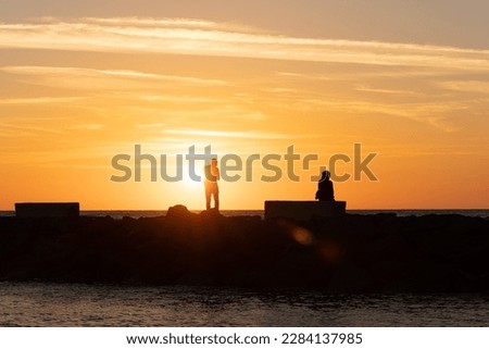 Man and women silhouetted against the sunset on the coast. Couple after a quarrel. Photo in the contur light. 