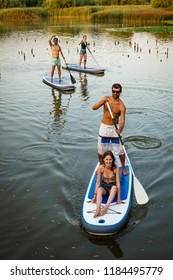 Man and women stand up paddleboarding on lake. Watersport on lake. Male and females tourists during summer vacation.
