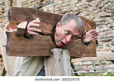 Man In Wooden Stocks From Medieval Times For Use With Prisoners, Criminals Or Witches As Public Punishment