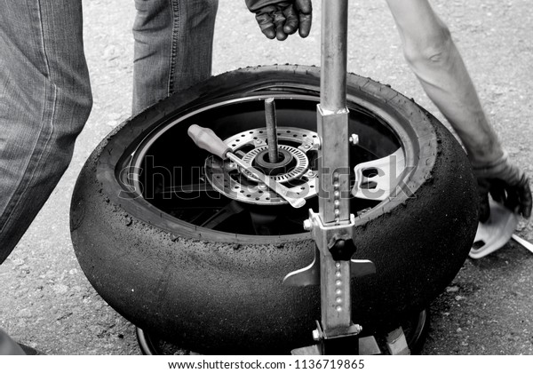 a man in work clothes and gloves repairing a wheel
from a motorcycle removing rubber on the tarmac, the theme of
repair and moto
