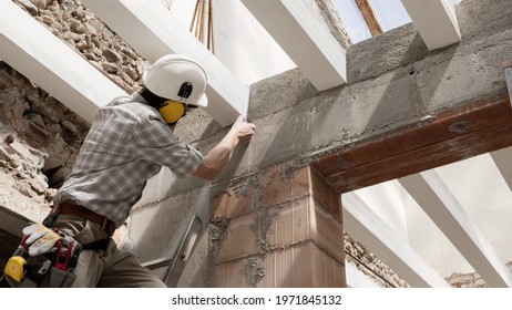 man at work, construction worker wear a helmet, check the measurements and distances of the beams at the base of the foundations of the second floor of house, in renovation building site background