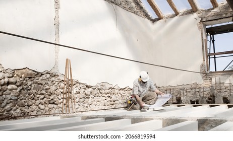 Man At Work, Construction Worker Wearing Helmet And Looking At Blueprint , Check The House Project Plan, In Renovation Building Site Background With The Beams At The Base Of The Foundations