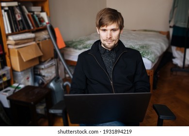 Man Work From Home In Small Apartment. Home Office In Small Apartment Bedroom. Male Using And Working From Laptop. Remote Online Business Worker. Virtual Meeting Call. Person Behind A Computer Screen