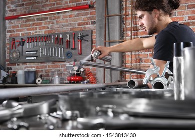 Man Work In Home Workshop Garage With Spray Can Paint Metal Pipe On The Workbench Full Of Wrenches, Diy And Craft Concept