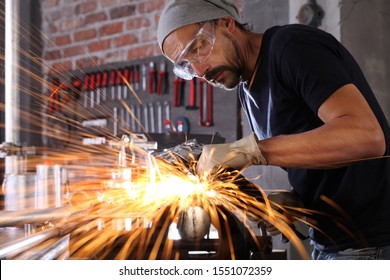 man work in home workshop garage with angle grinder, goggles and construction gloves, sanding metal makes sparks closeup, diy and craft concept - Powered by Shutterstock