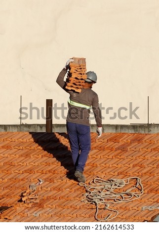 Man work on roofing installing. Roof constructin. Bricklayer roof repair. House under construction. Workman renovates waterproofing roof of building. Carpenter construction worker carry pile of tiles.