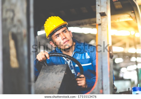 Man at work. Professional operation\
engineering. Young Asian worker forklift driver wearing safety\
goggles and hard hat sitting in vehicle in\
warehouse