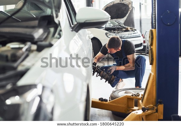 Man in work uniform repairs car indoors.\
Conception of automobile\
service.