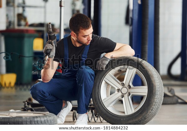 Man in work uniform sitting with car
wheel indoors. Conception of automobile
service.