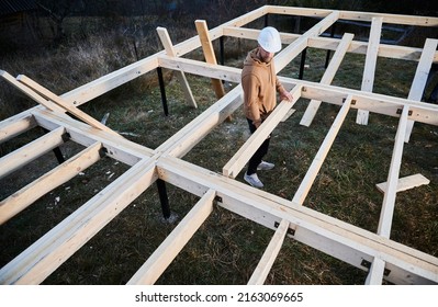 Man Worker Building Wooden Frame House On Pile Foundation. Carpenter Installing Wooden Truss For Timber Framing. Carpentry Concept.